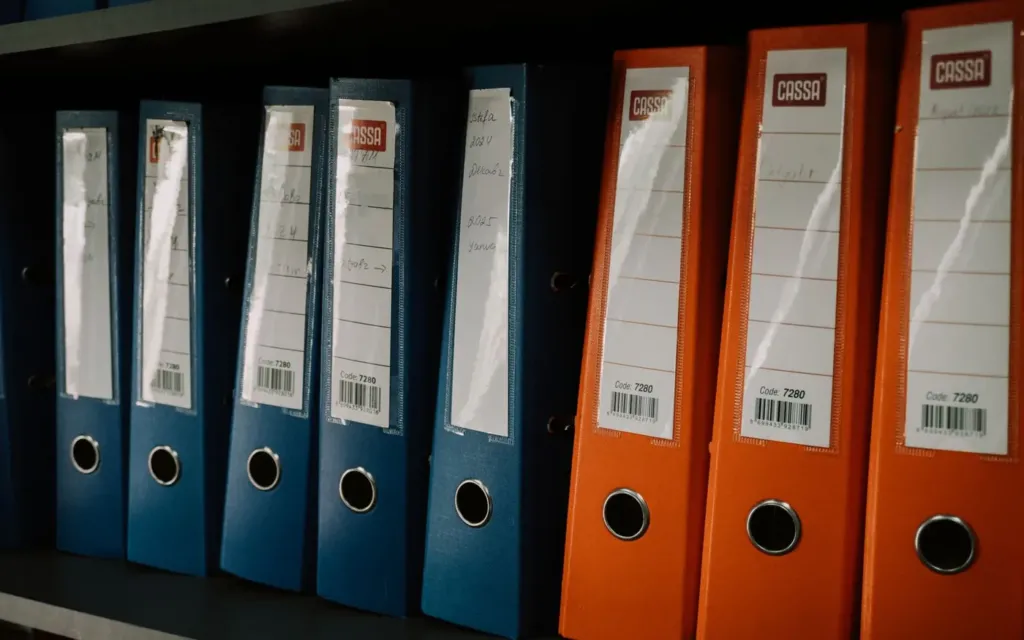 Rij blauwe en oranje ordners met etiketten in een archiefkast